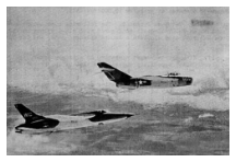 A black-and-white aerial photograph shows a MiG-17, marked with a U.S. insignia, flying alongside a U.S. Air Force F-105 Thunderchief over a layer of clouds.